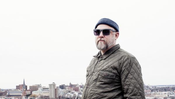 Portland Maine Dj and Flask Lounge Resident, Jamie O'Sullivan standing with the cityscape of Portland Maine behind him.